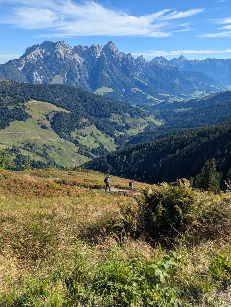 Zwei Wanderer folgen dem Saalachtaler Höhenweg mit eindrucksvoller Aussicht über das Glemmtal und die umliegenden Gipfel. Der Panoramaweg zählt zu den Highlights für Bergwanderer in Saalbach Hinterglemm im Sommer.