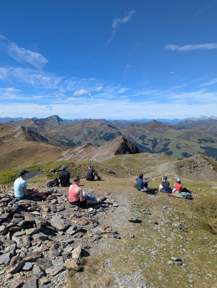 Eine Gruppe Wanderer macht Rast am Gipfel des Hochkogels oberhalb von Saalbach Hinterglemm. Von hier reicht der Blick weit über die Kitzbüheler Alpen.