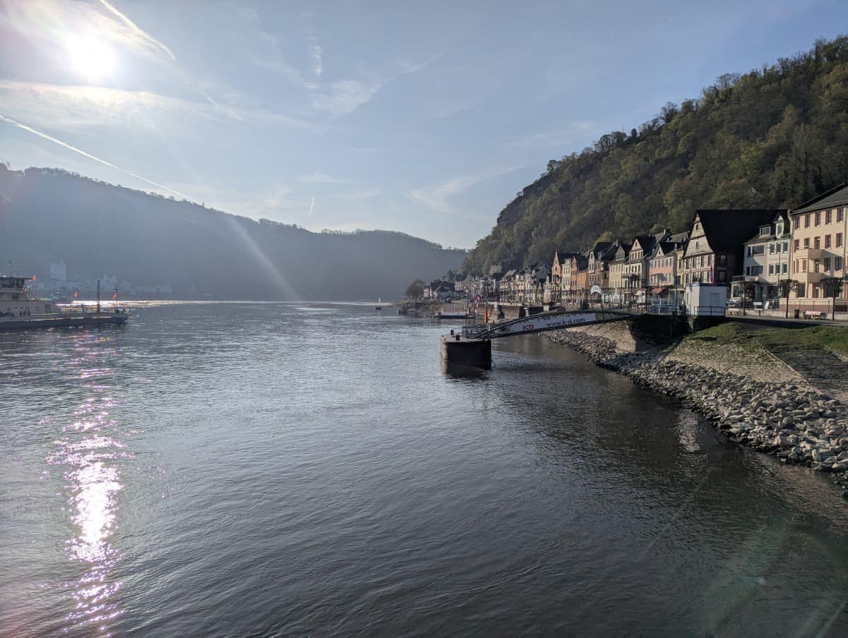 Blick vom Ufer in St. Goar auf den Rhein mit der Fähranlegestelle und den historischen Häusern entlang der Uferpromenade im Mittelrheintal. Per Fähre lassen sich Rheinsteig und RheinBurgenWeg gut verbinden.