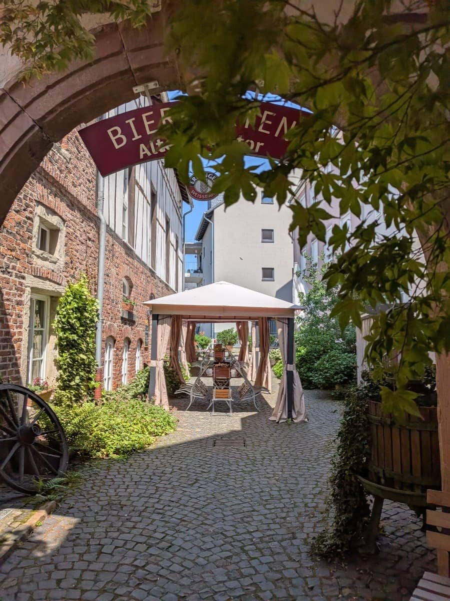 Der gemütliche Innenhof des Hotel & Landgasthaus Altes Stadttor in Kastellaun lädt mit historischem Mauerwerk, Kopfsteinpflaster und schattigen Sitzplätzen zum Verweilen ein.