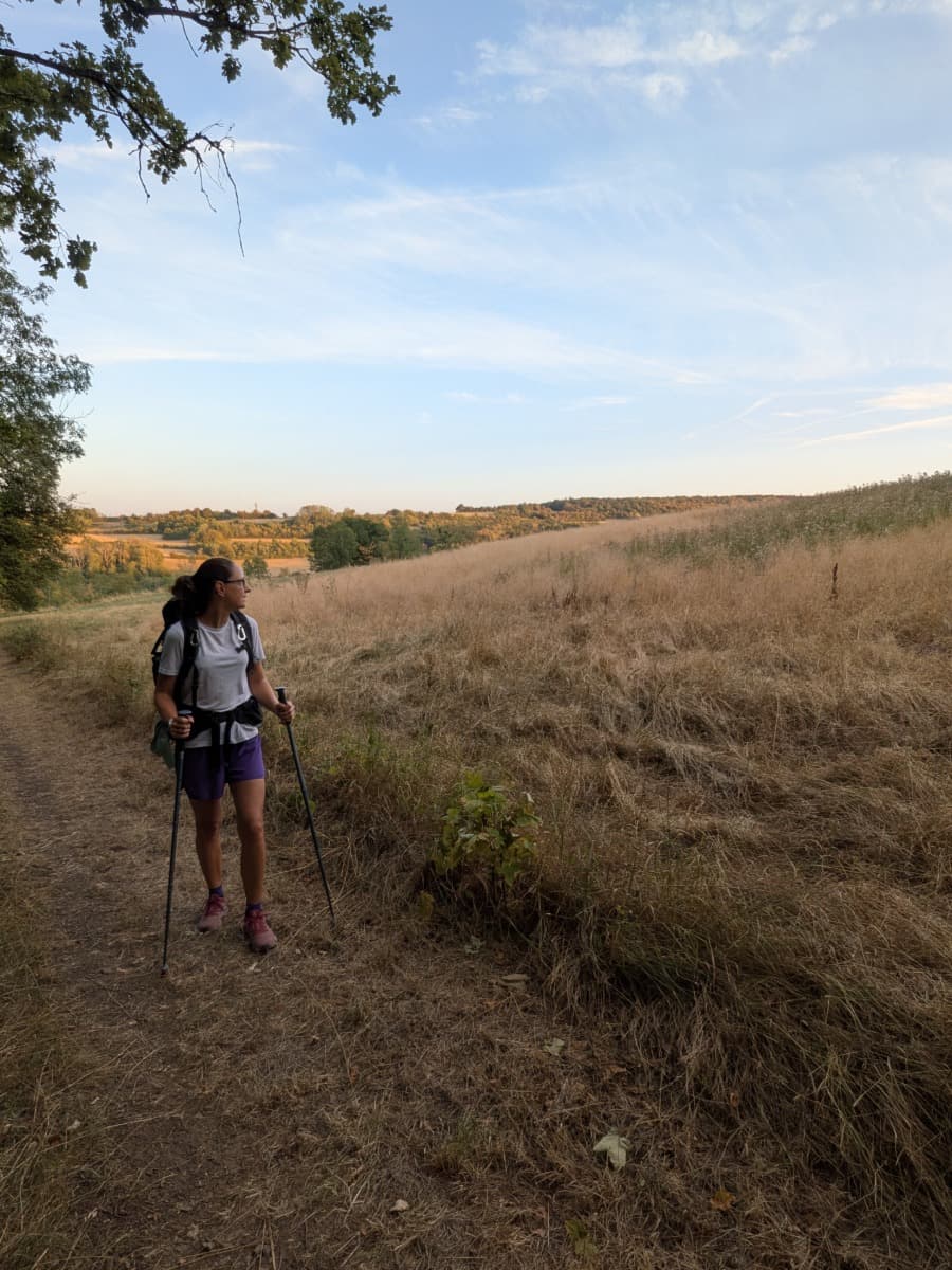Linda wandert mit Trekkingstöcken durch trockene Wiesen und Felder der typischen Bliesgau-Landschaft auf dem Bliessteig im Saarland.