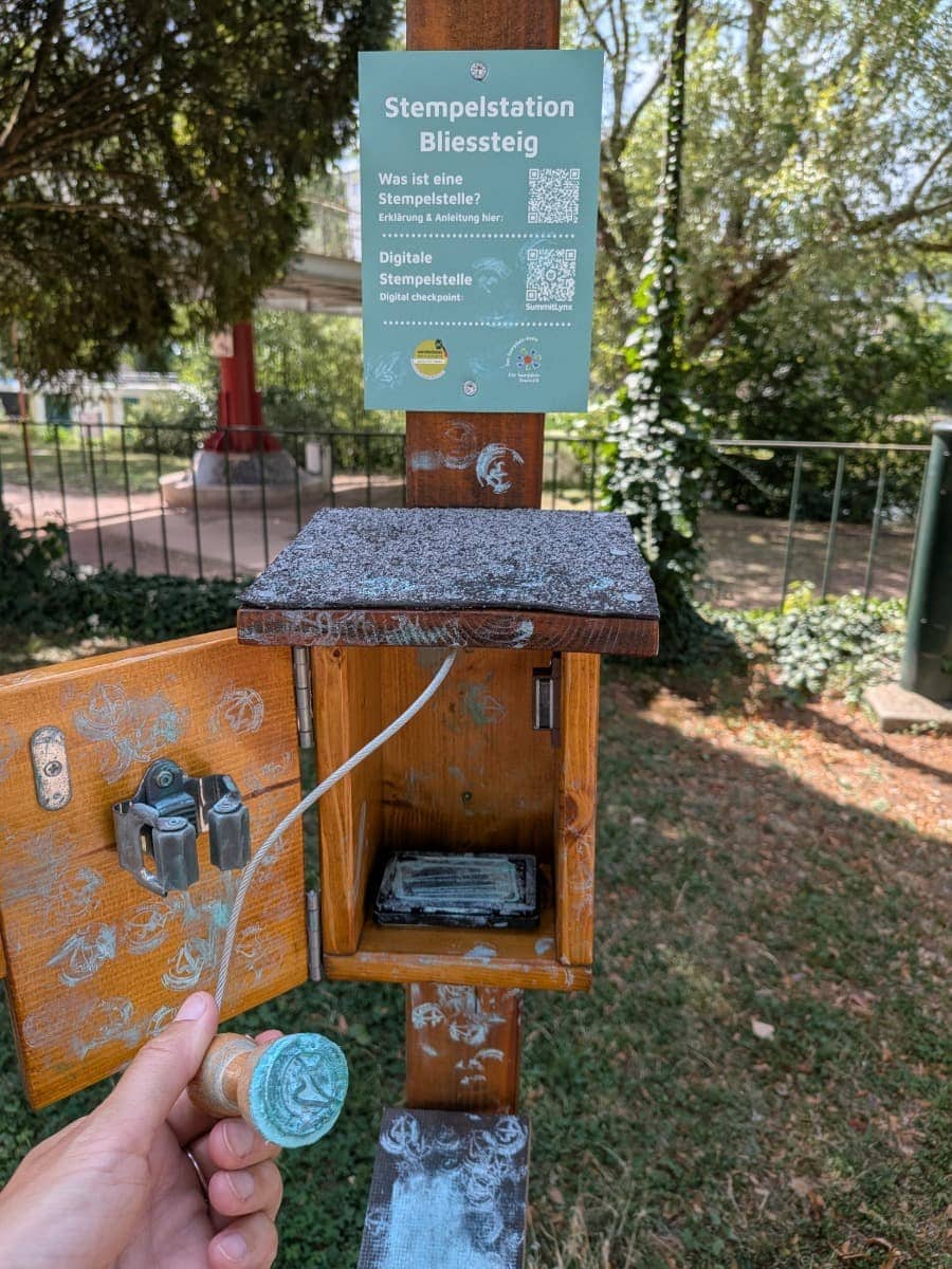 Eine hölzerne Stempelstation mit Wanderstempel markiert einen Kontrollpunkt auf dem Bliessteig.