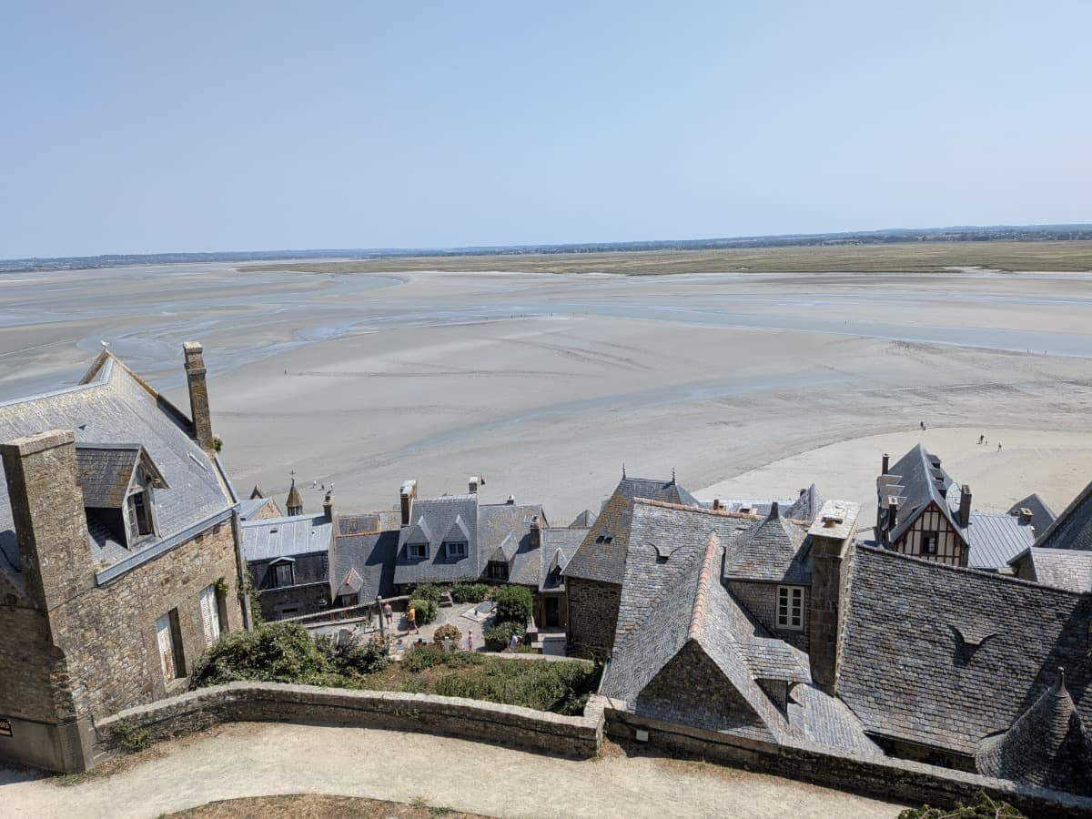 Blick von den Wehrmauern des Mont-Saint-Michel über die Dächer der mittelalterlichen Insel und das bei Ebbe freiliegende Watt der Baie du Mont-Saint-Michel.
