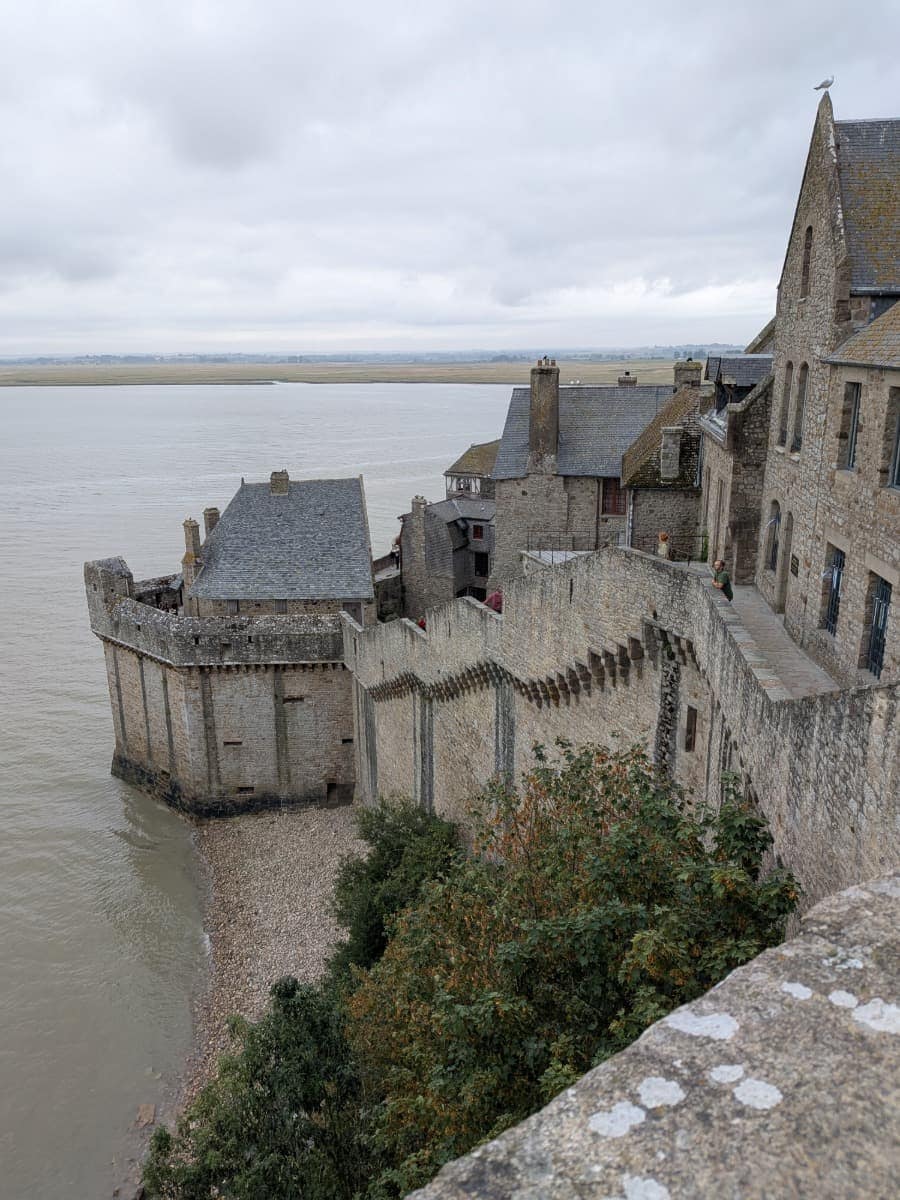 Die Wehrmauern des Mont-Saint-Michel verlaufen entlang der historischen Gebäude und bieten einen weiten Blick über die Bucht Baie du Mont-Saint-Michel.