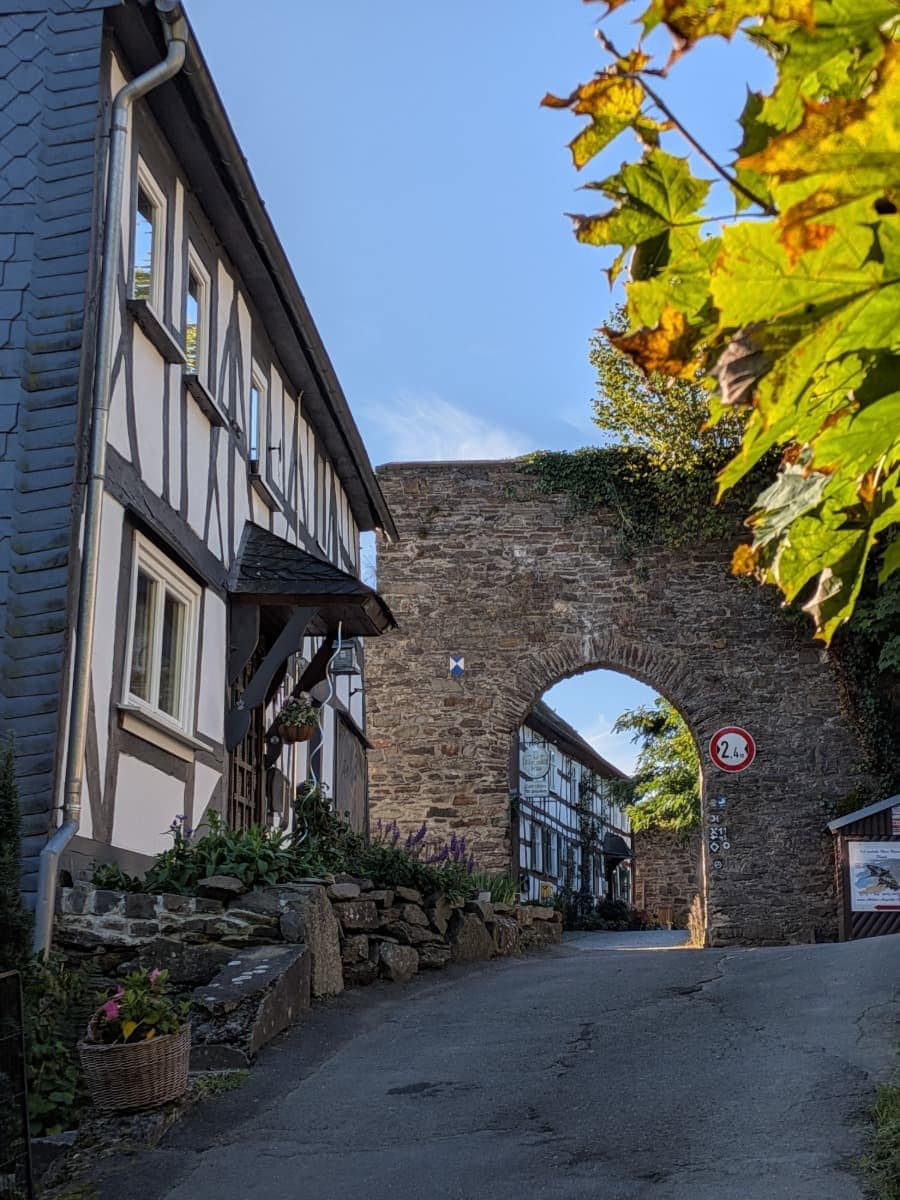 Im Ortskern von Freusburg führt eine schmale Gasse zwischen Fachwerkhäusern durch einen steinernen Torbogen am Druidensteig.