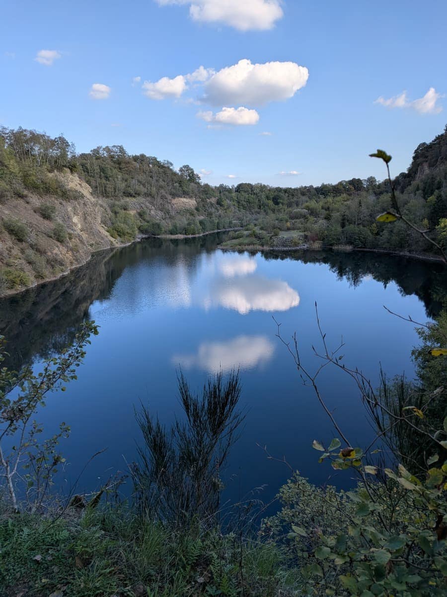 Im Silbersee auf der Mahlscheid am Druidensteig im Westerwald spiegeln sich weiße Wolken und die bewaldeten Hänge des ehemaligen Steinbruchs.
