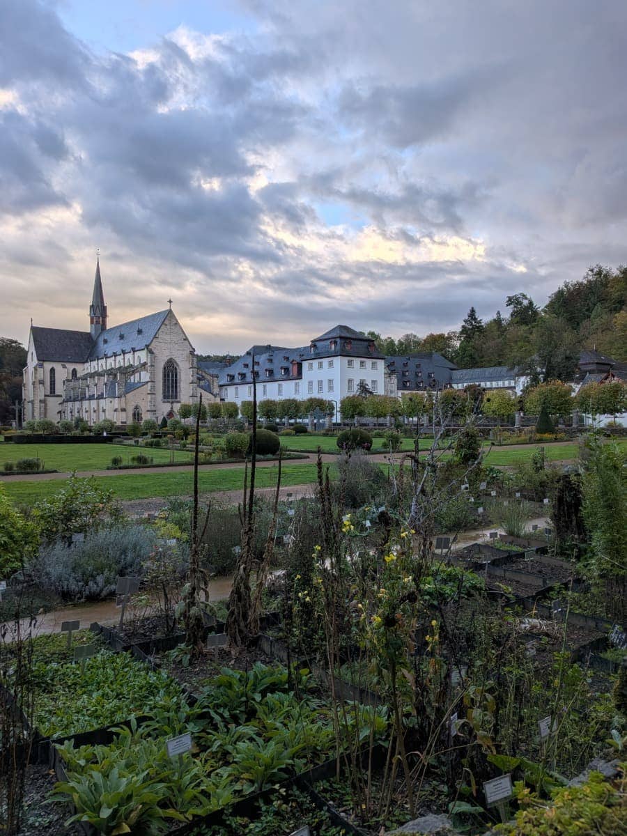 Hinter den bepflanzten Beeten des Klostergartens stehen die Kirche und die weißen Gebäude der Abtei Marienstatt am Druidensteig.