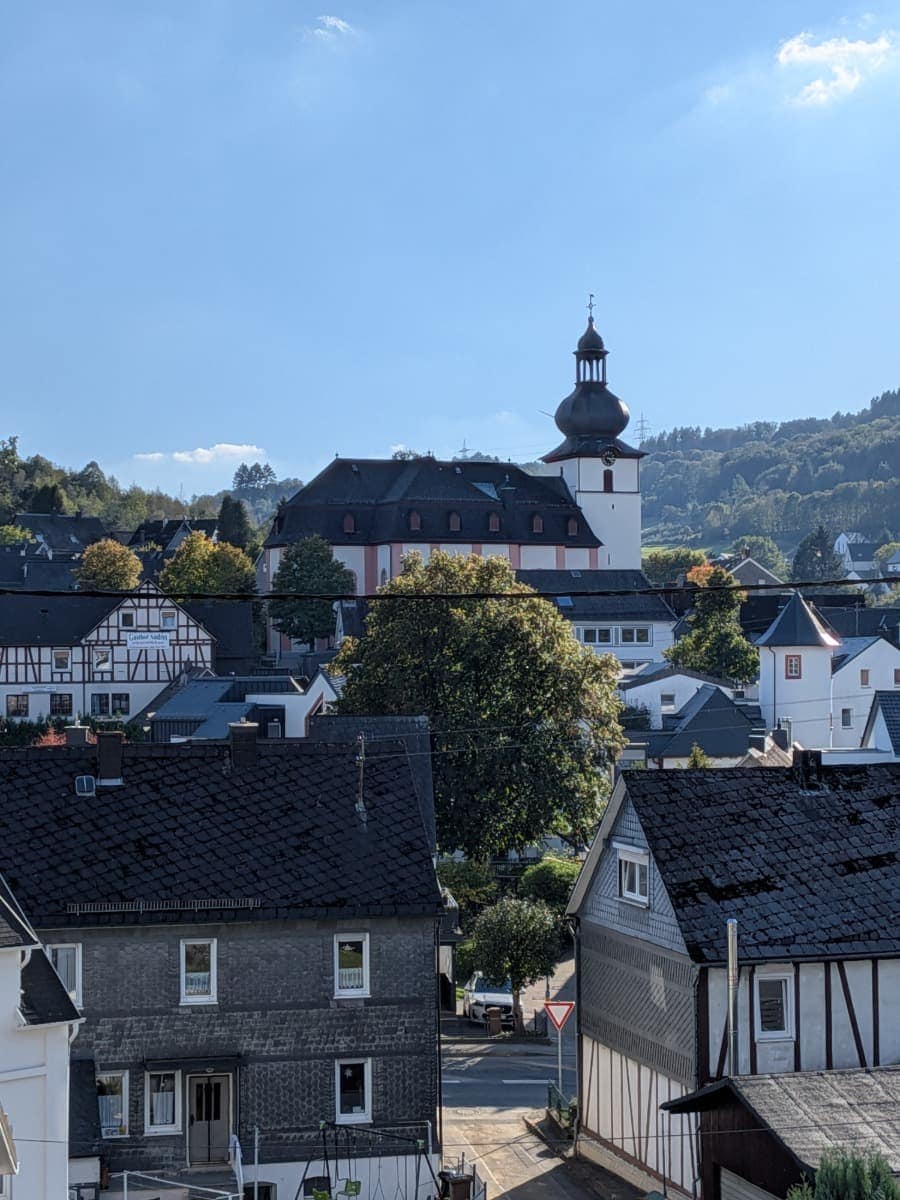 Die Barockkirche mit ihrem Zwiebelturm erhebt sich in Daaden über Fachwerkhäuser und dunkle Schieferdächer.