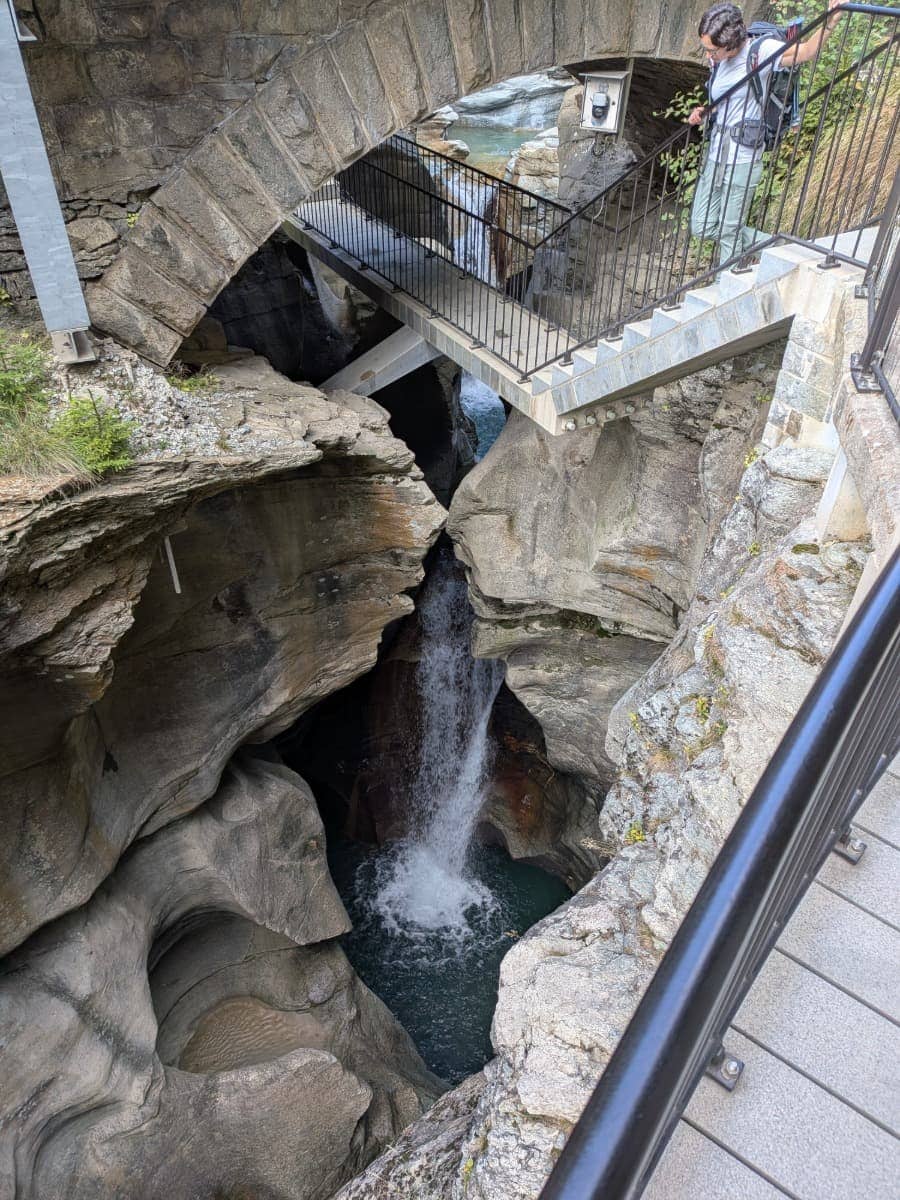 Linda blickt im Gletschergarten Cavaglia in eine tief ausgeschliffene Felsschlucht mit Wasserfall und türkisfarbenem Wasser, die durch jahrtausendelange Gletschererosion geformt wurde.