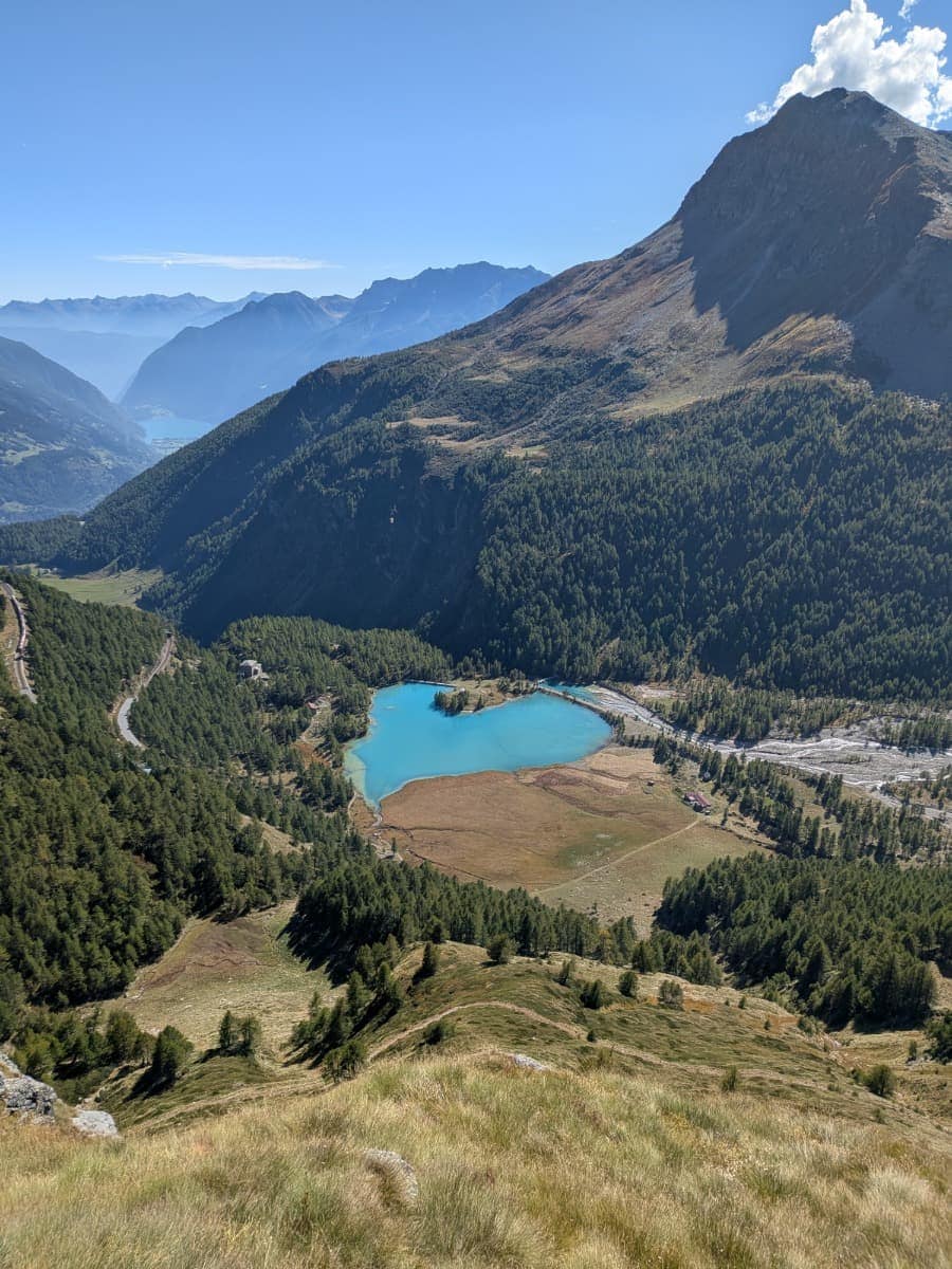 Vom Höhenweg öffnet sich der Blick hinunter auf den türkisfarbenen Lagh da Palü bei Alp Grüm, während in der Ferne das Puschlav und der Lago di Poschiavo zwischen den Bergen liegen.