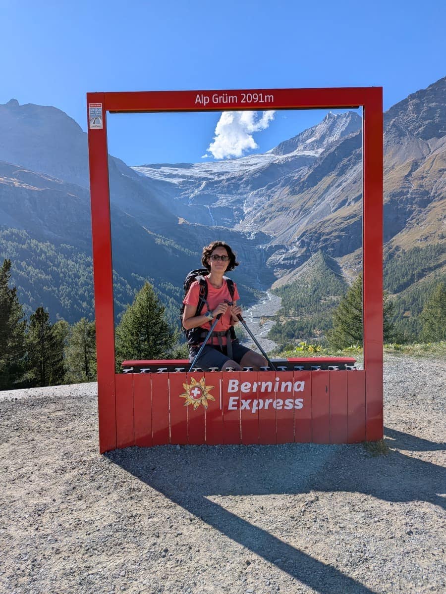 Linda sitzt im roten Fotofenster von Alp Grüm auf 2091 Metern, direkt vor dem Palügletscher (Vadret da Palü) und den steilen Gipfeln der Piz-Palü-Gruppe.